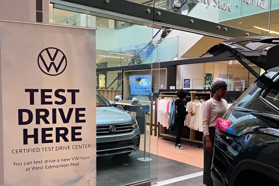 A close-up of a "Test Drive Here" sign, highlighting a silver SUV and a lifestyle clothing rack inside the boutique.