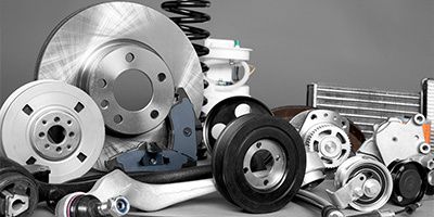 A wide assortment of new automotive components, including brake rotors, pads, a suspension spring, and various pulleys, arranged against a grey background.