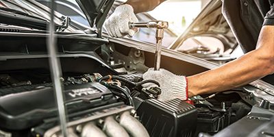 A close-up of a mechanic's gloved hands using a torque wrench to tighten a bolt on a car engine under an open hood.