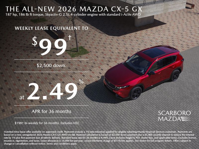 Smiling man wearing a red blazer, standing in a car dealership showroom.