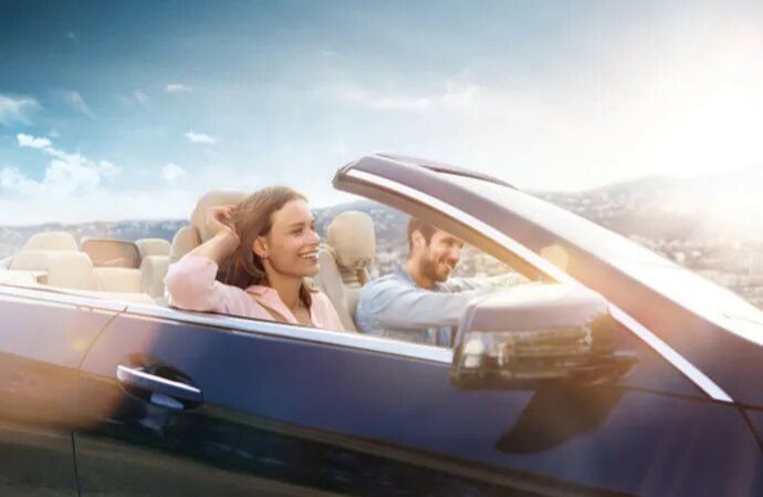 A smiling couple driving in a convertible car on a sunny day.