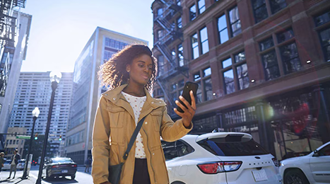 Woman walking in the city using her smartphone to lock or unlock her Ford vehicle.