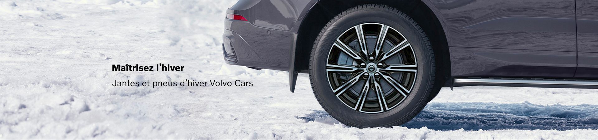 Gros plan sur une roue d'hiver de Volvo (pneu et jante en alliage) en gros plan, avec de la neige et de la glace en arrière-plan.