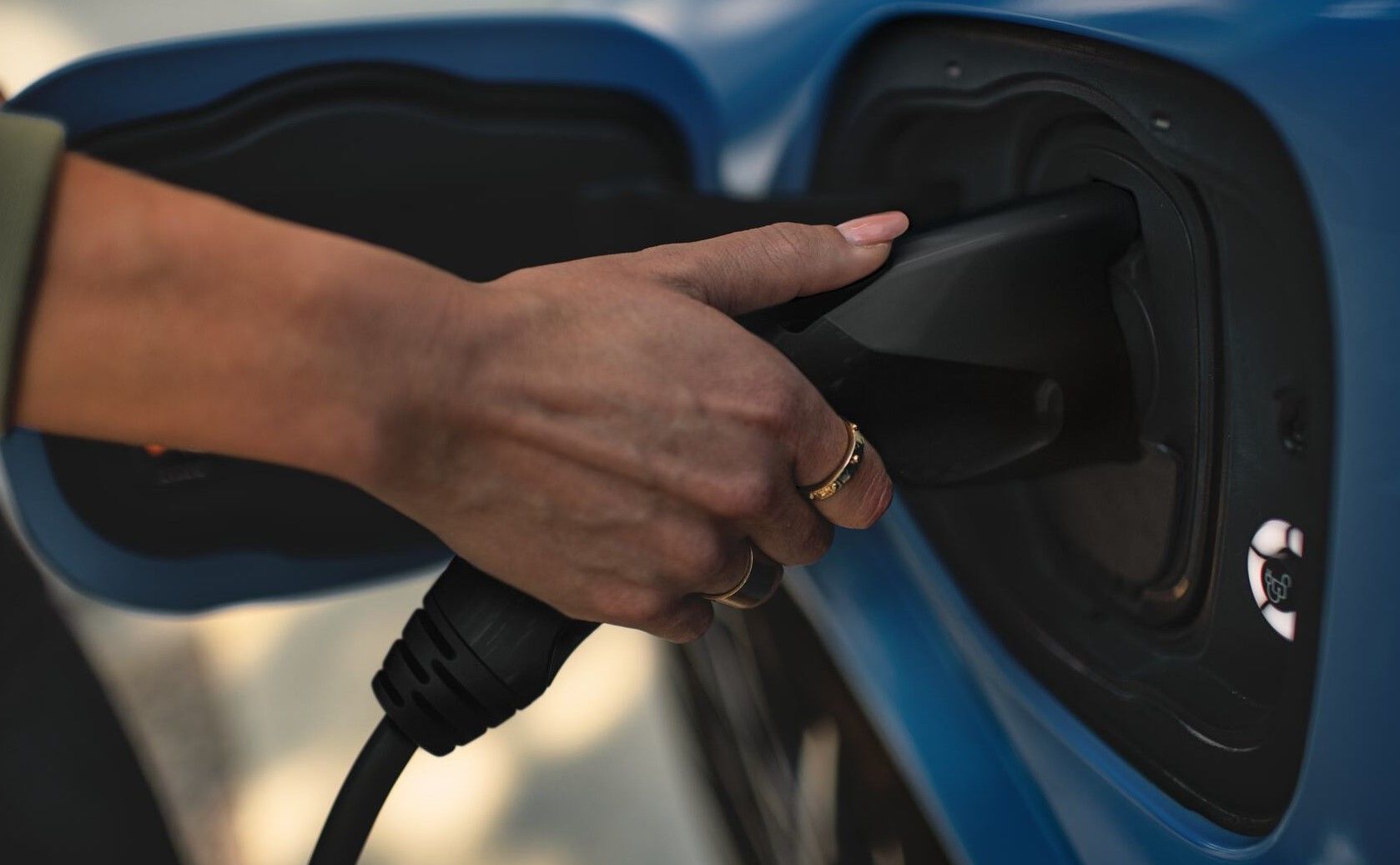 Close-up of a hand plugging in a charger into a charging port of a vehicle.