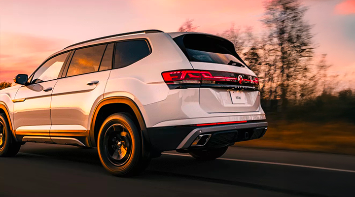 Rear view of a white Volkswagen Atlas SUV driving on a road at sunset, highlighting the 4MOTION All-Wheel Drive system.