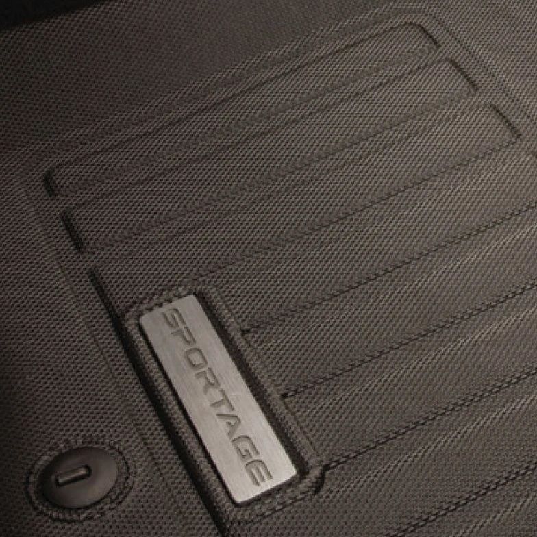 Un gros plan d'un tapis de sol toutes saisons noir et texturé, arborant une plaque argentée avec le mot « SPORTAGE ».