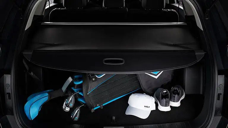 The trunk of an SUV with the retractable cargo cover partially open, revealing a golf bag, a cap, and shoes underneath.