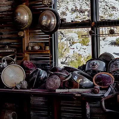 A cluttered workbench in a rustic shed, covered with a collection of vintage car headlights, with a snowy landscape visible through the window.
