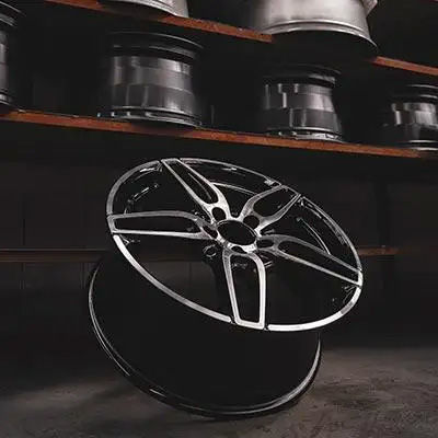 A modern, multi-spoke alloy wheel with a black and machined silver finish, showcased in front of a shelf holding more wheels.