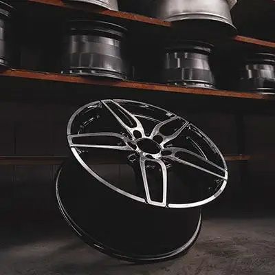 A modern, multi-spoke alloy wheel with a black and machined silver finish, showcased in front of a shelf holding more wheels.