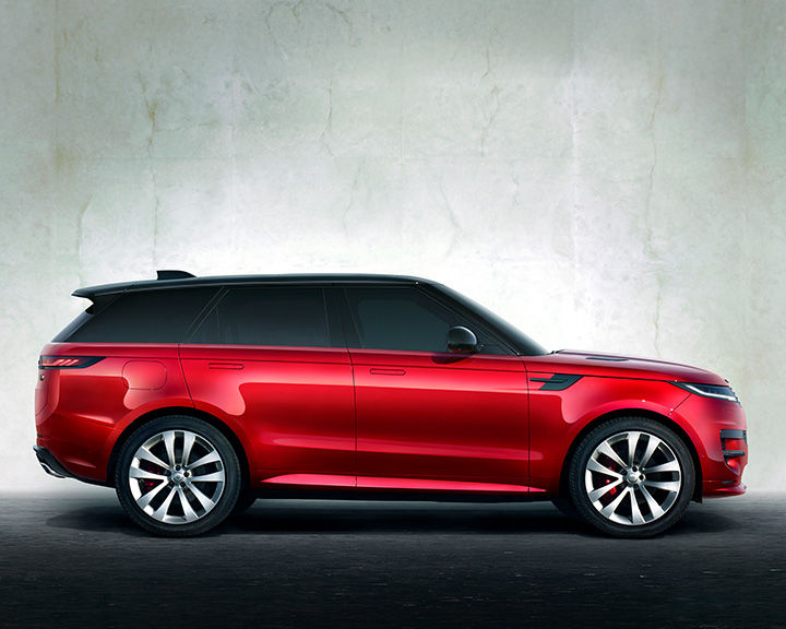 Side profile of a vibrant red Range Rover Sport with a black roof, parked against a textured light grey wall.