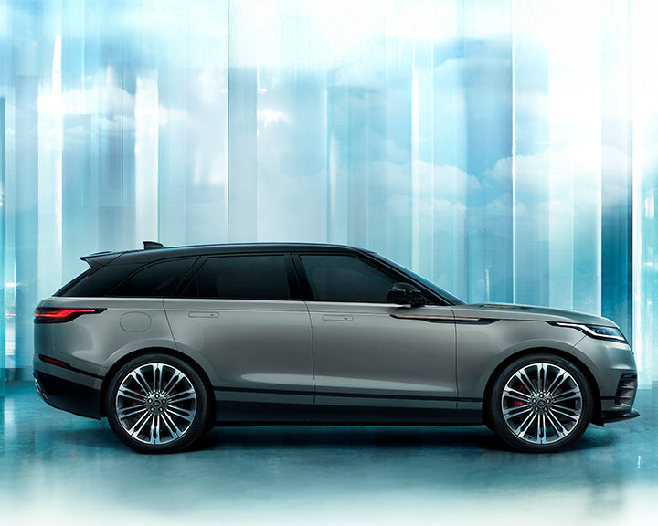 Side profile of a silver Range Rover Velar with a black roof, set against a blurred, abstract background of blue and white vertical streaks.
