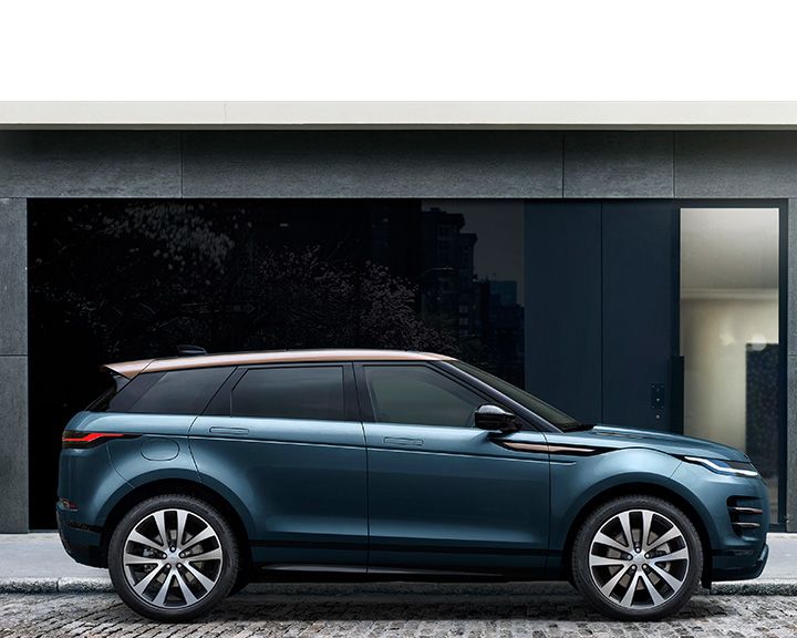 Side profile of a metallic teal Land Rover Evoque with a contrasting copper-colored roof, parked in front of a modern dark building facade.