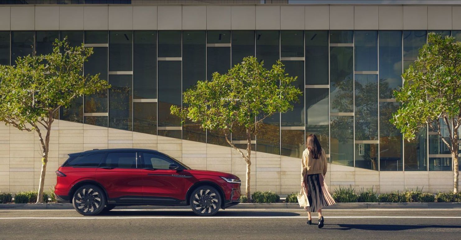 A red Lincoln Corsair SUV parked beside a modern building, with a woman walking away from it.