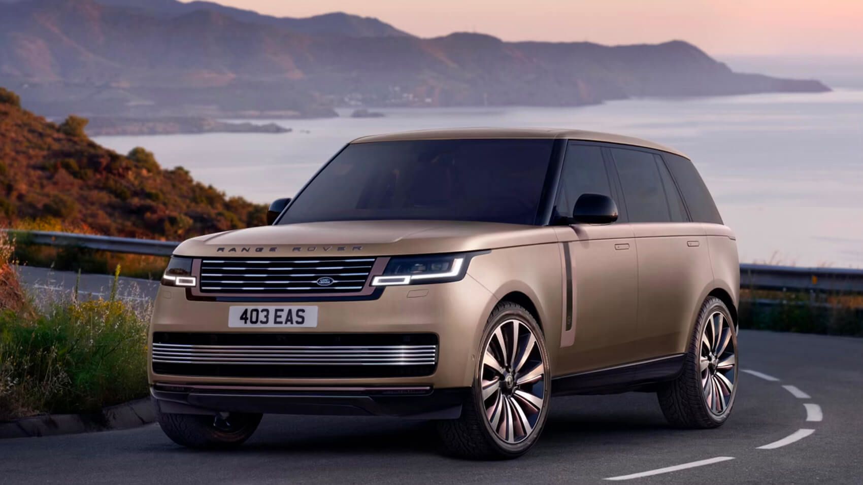 Front three-quarter view of a champagne-gold Range Rover parked on a coastal road at sunset.
