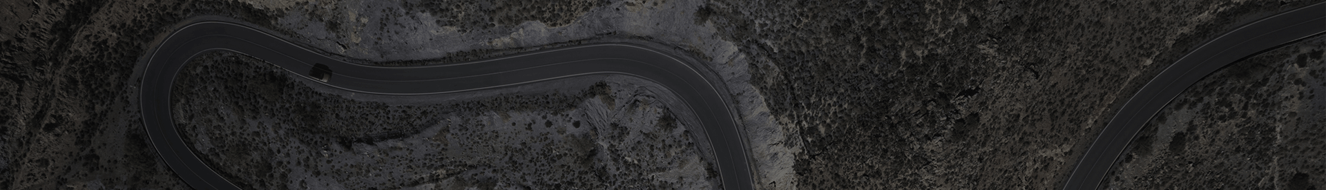Aerial view of a winding asphalt road cutting through a dark, rocky terrain.