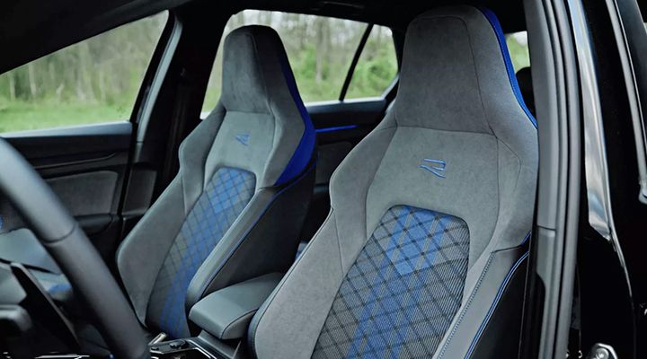 Interior view showing the sport seats of a Volkswagen Golf R with blue and gray cloth upholstery and the embroidered R logo.