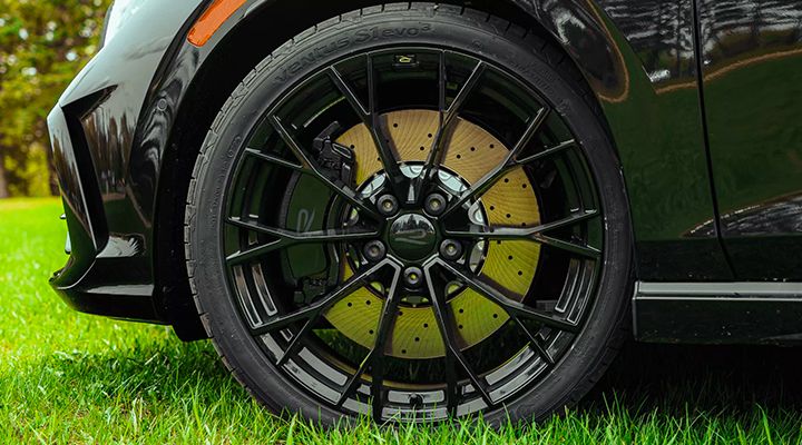 Close-up of a car's black performance wheel, showing the multi-spoke rim and perforated brake rotors.