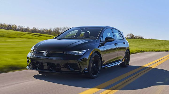 A black Volkswagen Golf R Black Edition hatchback drives on a sunny country road.