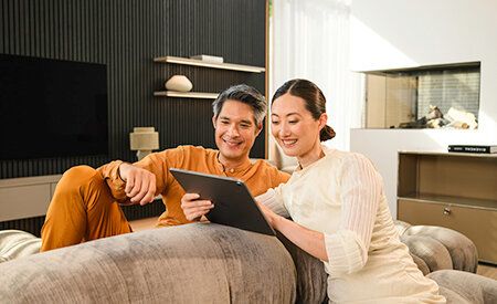 A smiling couple sitting on a sofa looking at content together on a digital tablet.