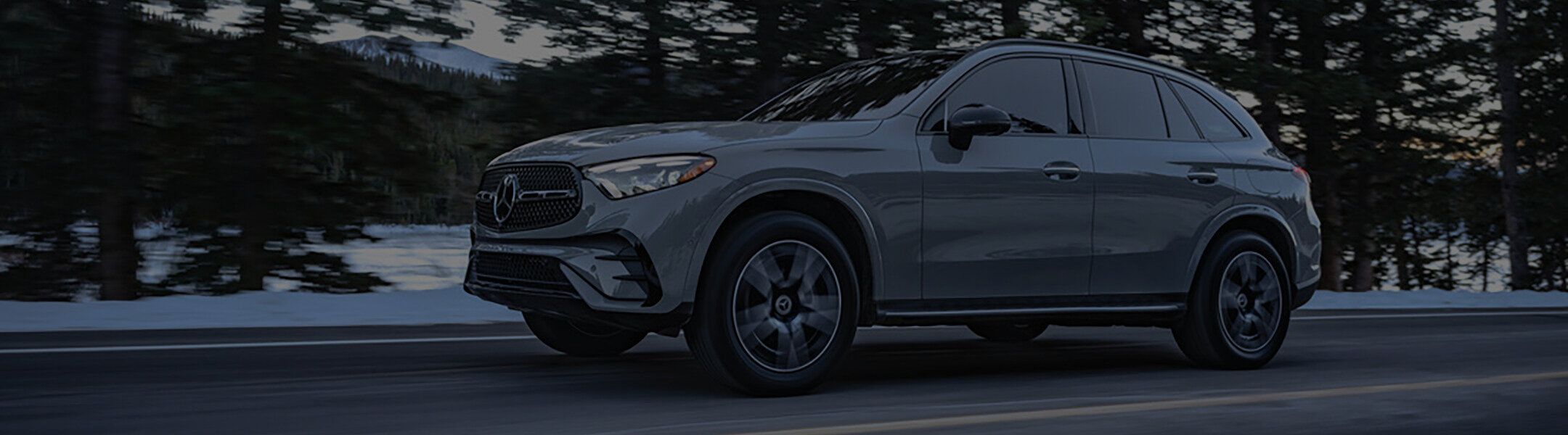 Grey Mercedes-Benz GLC driving on a snowy road through a conifer forest