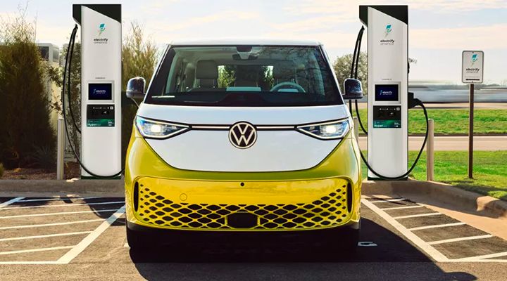 Vue de face d'une fourgonnette électrique Volkswagen ID. Buzz bicolore jaune et blanc, garée entre deux bornes de recharge Electrify Canada.