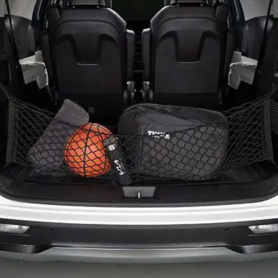 A cargo net stretched across the open trunk of a vehicle, holding a basketball, a water bottle, and some bags in place.