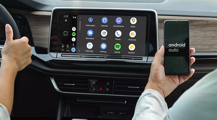 A passenger holds up a mobile phone next to the infotainment screen, which displays the Android Auto interface.