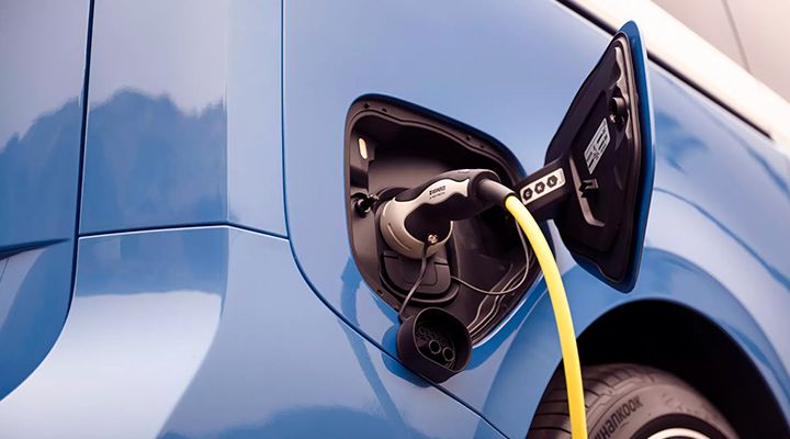 Gros plan sur une prise de charge branchée au port de charge ouvert d'un véhicule électrique bleu.