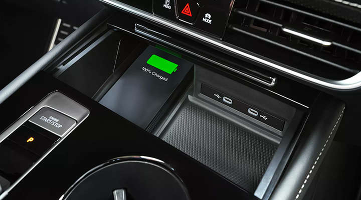 Close-up of a car's center console, showing a smartphone wirelessly charging in a storage compartment.