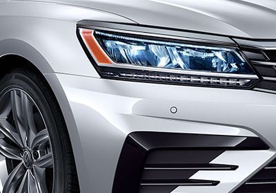 Gros plan du phare avant à LED et de la calandre d'une Volkswagen de couleur argent, mettant en évidence les capteurs de stationnement.