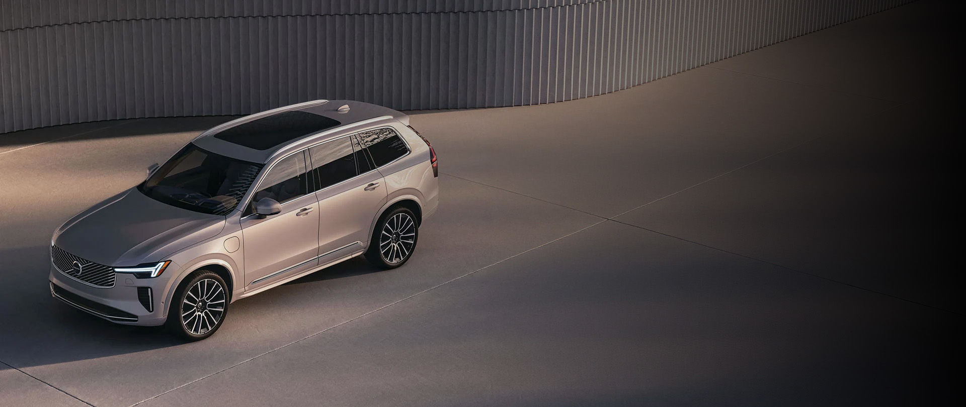 Vue en plongée d'un Volvo EX90 argenté stationné sur une surface en béton à côté d'un mur moderne à nervures.