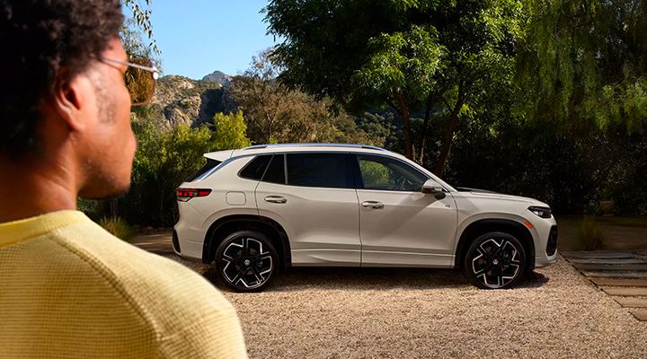 Side view of a light beige Volkswagen SUV parked on gravel, with a man facing away in the foreground looking at the vehicle.