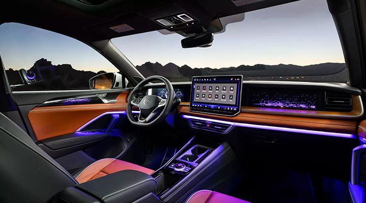Interior view of the cockpit at night, highlighting the brown leather-trimmed dashboard, blue/purple ambient lighting, and the large central infotainment screen.