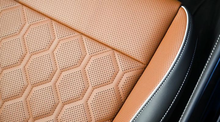 Close-up of the hexagonal perforated pattern on the brown leather seating surface, with black leather accents and white contrast stitching.