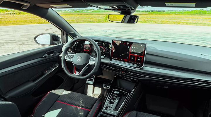 Interior view of the cockpit of a Volkswagen Golf GTI, showing the steering wheel, the digital dashboard, and the large touchscreen infotainment system.