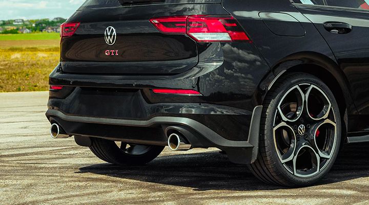 Close-up on the rear bumper and dual exhaust of a black Volkswagen Golf GTI, showing the GTI badge, the wheel, and the diffuser.
