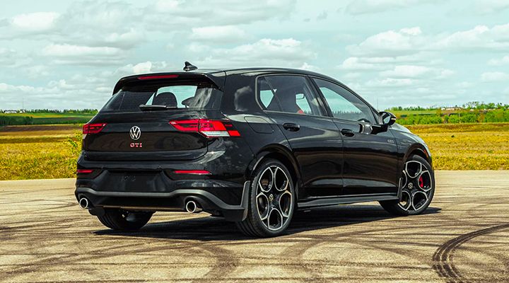 Rear and side view of a black Volkswagen Golf GTI, parked on an asphalt lot with tire marks and a cloudy sky in the background.