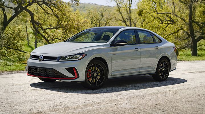 Une Jetta GLI blanche stationnée sur une route panoramique avec des arbres et des collines herbeuses en arrière-plan.
