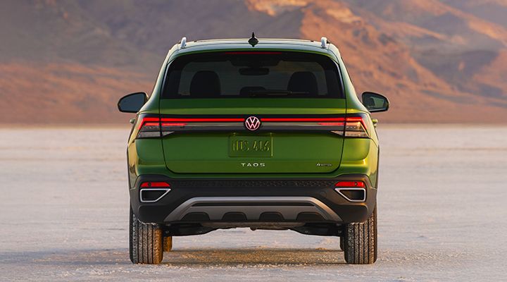 Rear view of a green 2026 Volkswagen Taos parked on a dirt road overlooking a mountainous landscape.