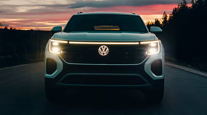 Front view of a Volkswagen Atlas or Atlas Cross Sport at night or twilight, highlighting the full-width front LED light bar and headlights.