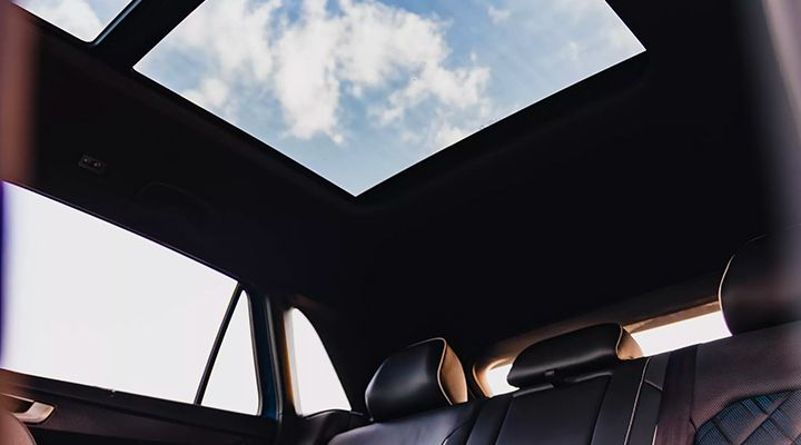 Interior view looking up, showing the large panoramic sunroof and blue sky with clouds.
