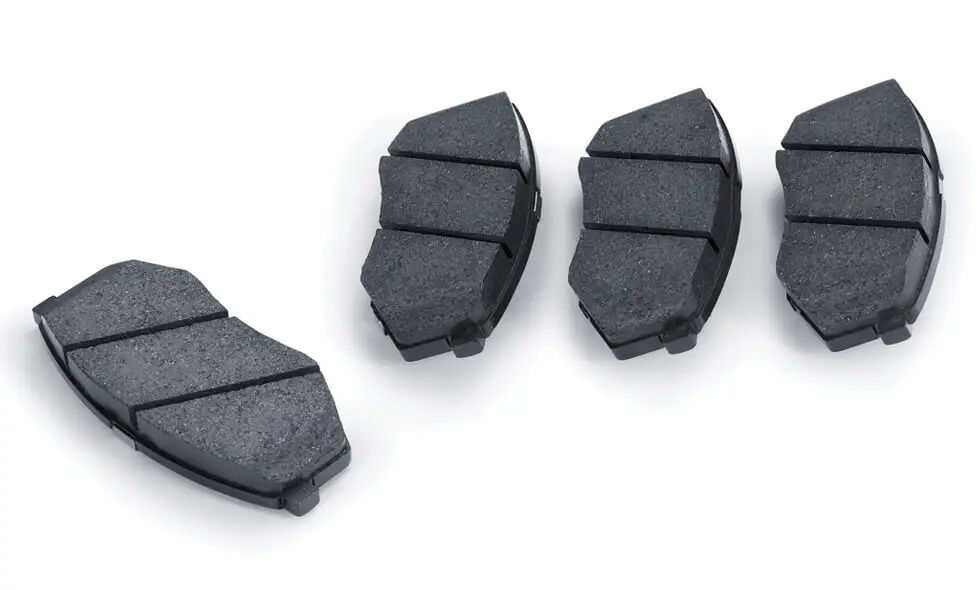 A set of four new, black automotive brake pads laid out on a white background.
