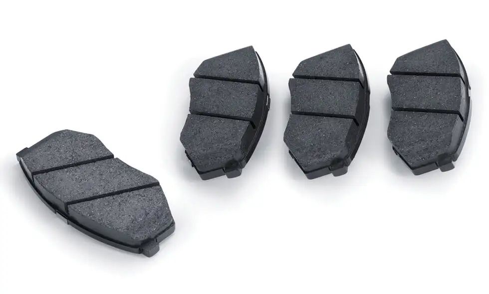 Un jeu de quatre plaquettes de frein automobiles neuves et noires, disposées sur un fond blanc.         Show thinking