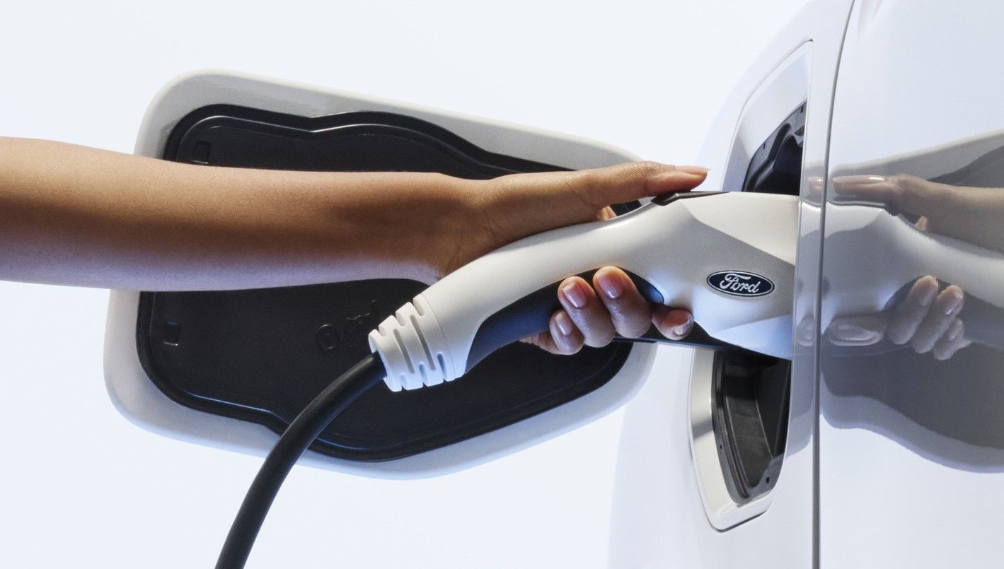 Hand inserting a Ford-branded charging cable into an electric vehicle's charging port.