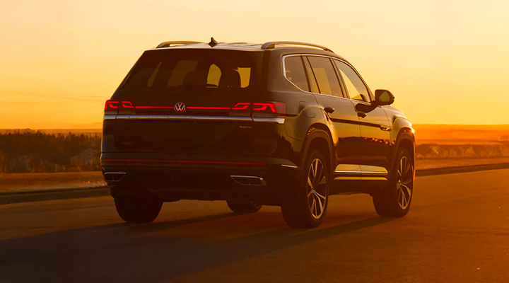 Vue arrière d'un VUS Volkswagen Atlas noir roulant sur une route sous la lumière intense du coucher du soleil.