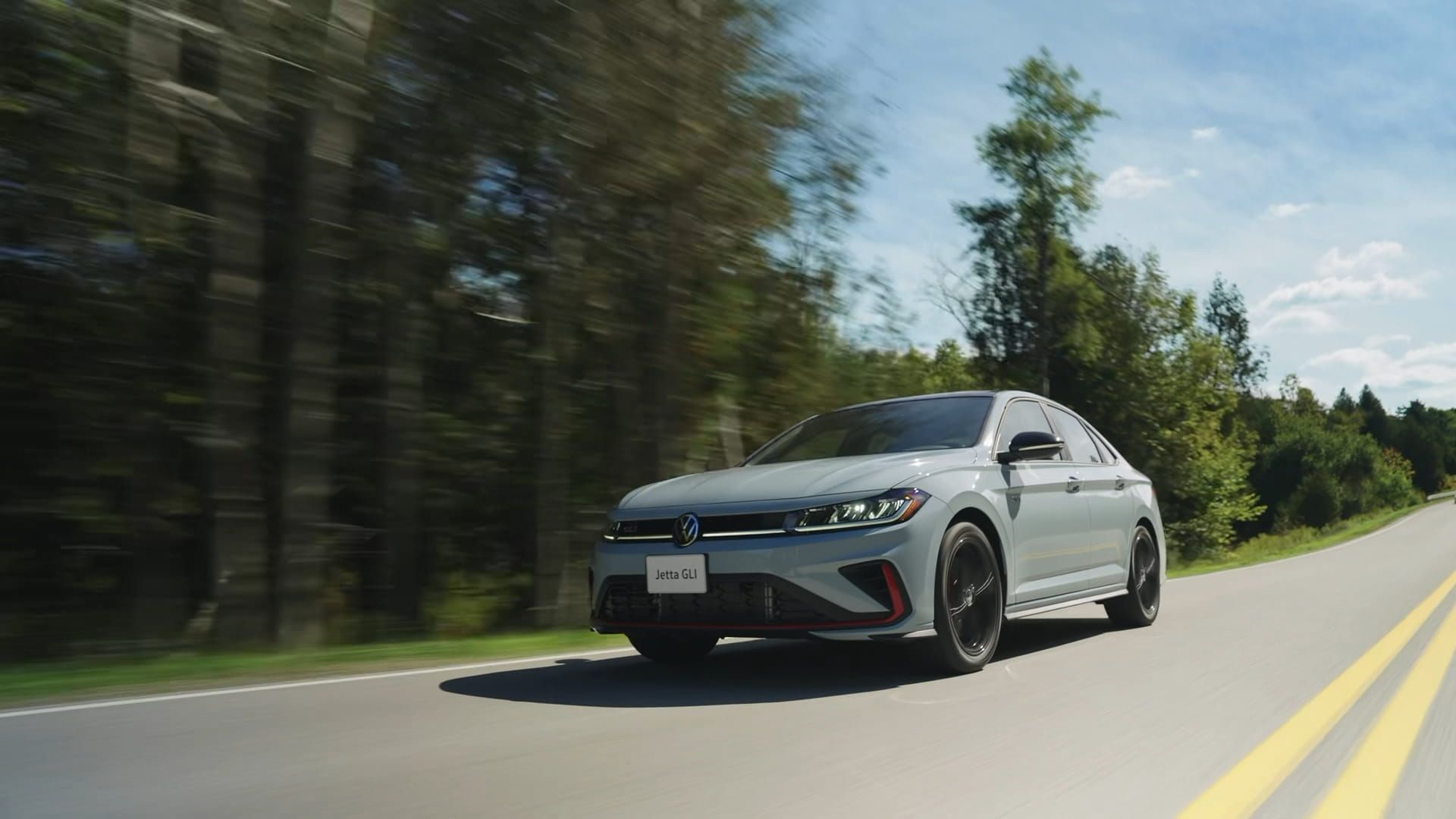 Jetta GLI driving on a scenic road with trees in the background.