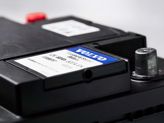 A close-up of a Genuine Volvo car battery, showing the blue Volvo label and the battery terminals