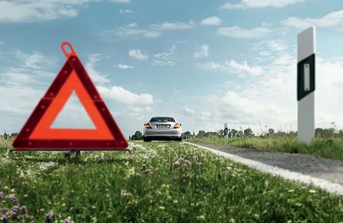 A red warning triangle placed on the side of a road with a car parked in the distance.