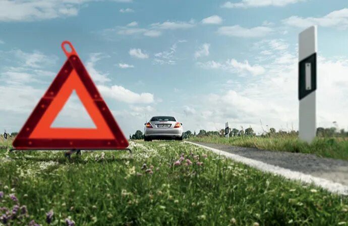 Warning triangle on the roadside with a Mercedes-Benz broken down in the background